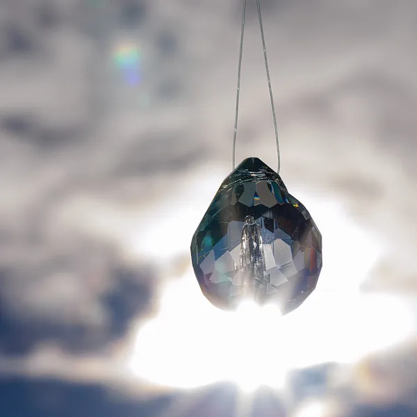 Faceted glass teardrop pendant backlit by the sun
