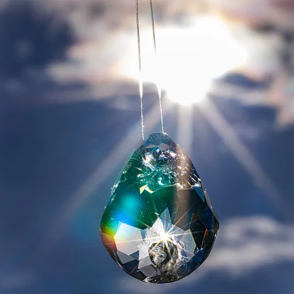 Faceted glass teardrop pendant backlit by the sun
