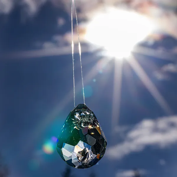 Faceted glass teardrop pendant backlit by the sun